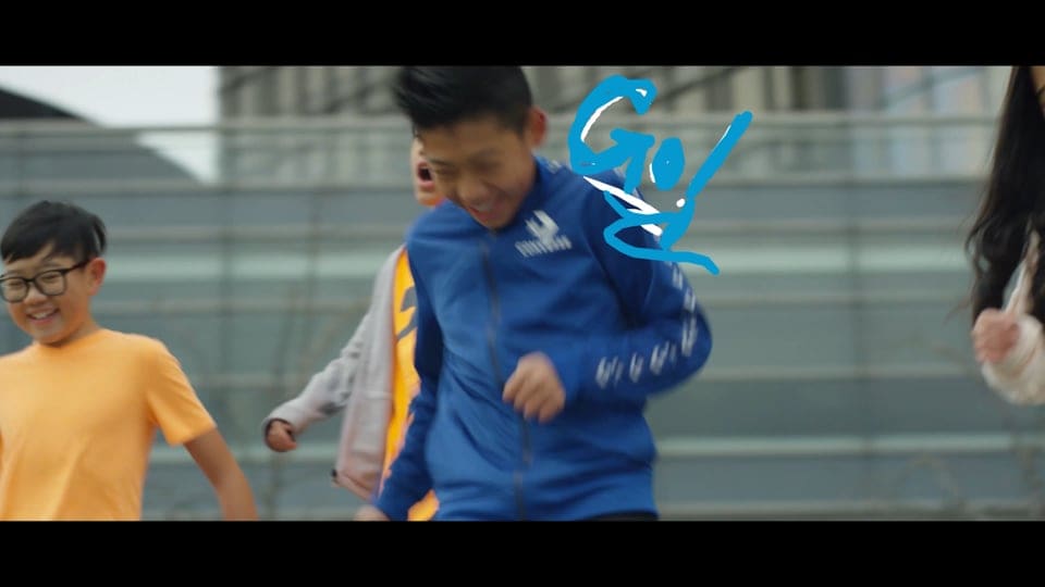 Photo of young boys running and playing soccer together on an outside field. Next to one of the boys is blue handwritten text that says "Go!"