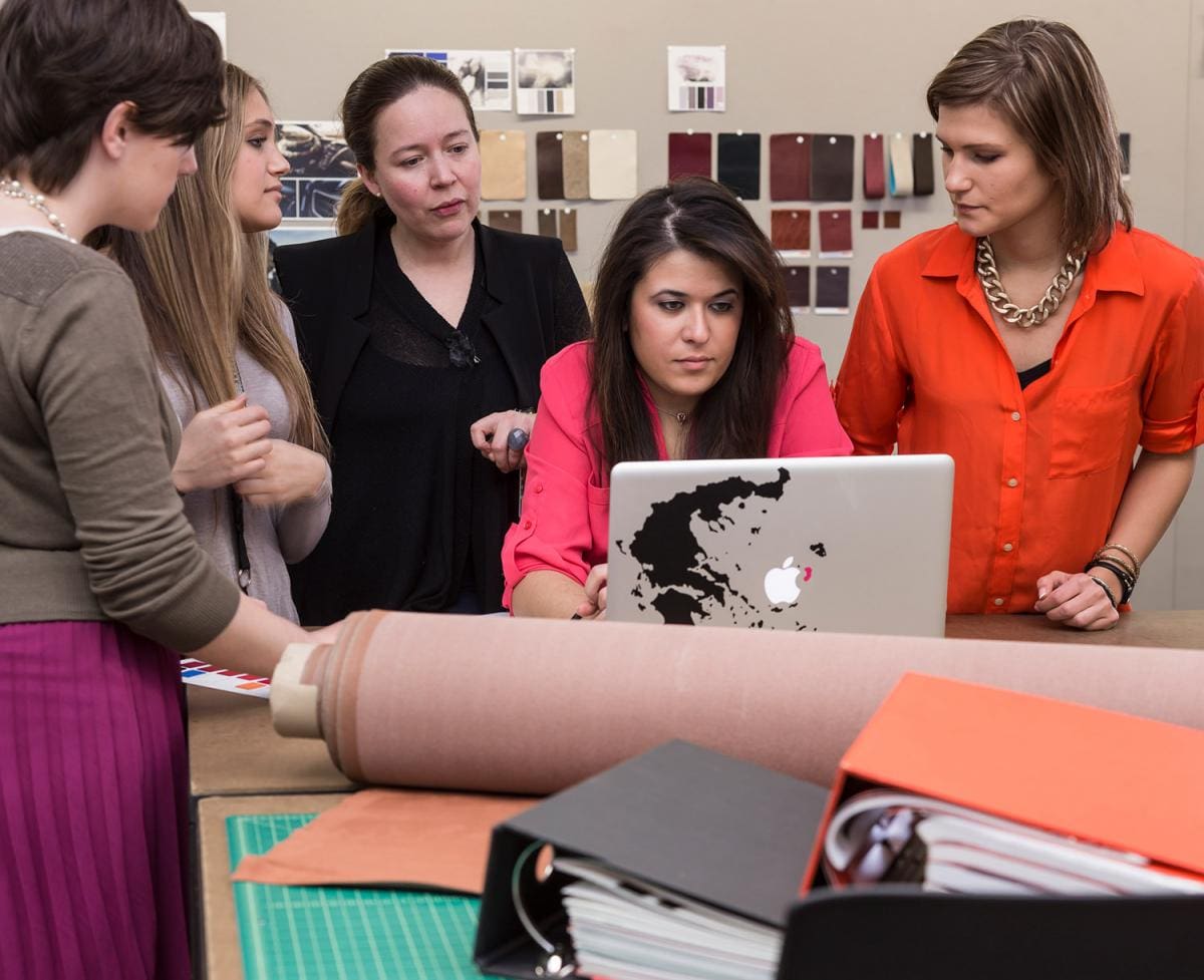 Photo of five Interior Design students working together on a laptop in a classroom.