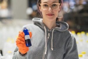 Smiling woman in grey hoodie holding up a bottle of sanitizer