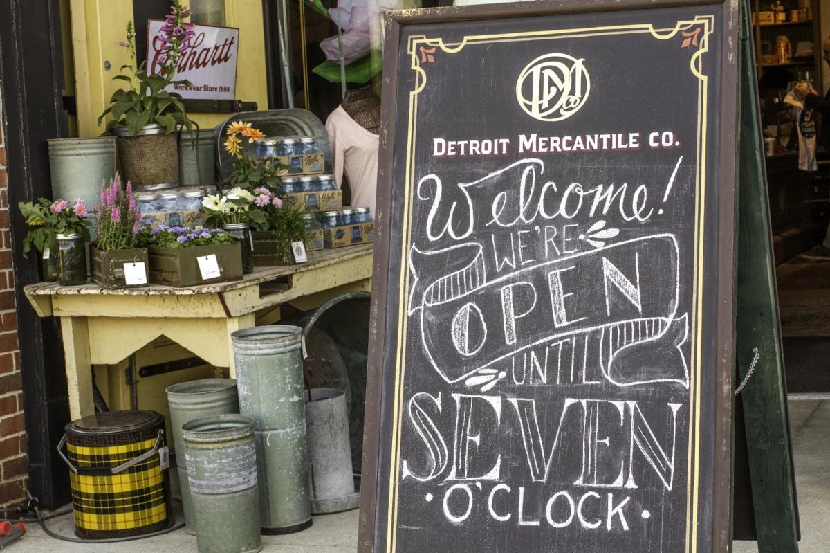 Photo of a chalkboard written with the words "Welcome! We're open until Seven O'clock" outside a flower boutique in Detroit.