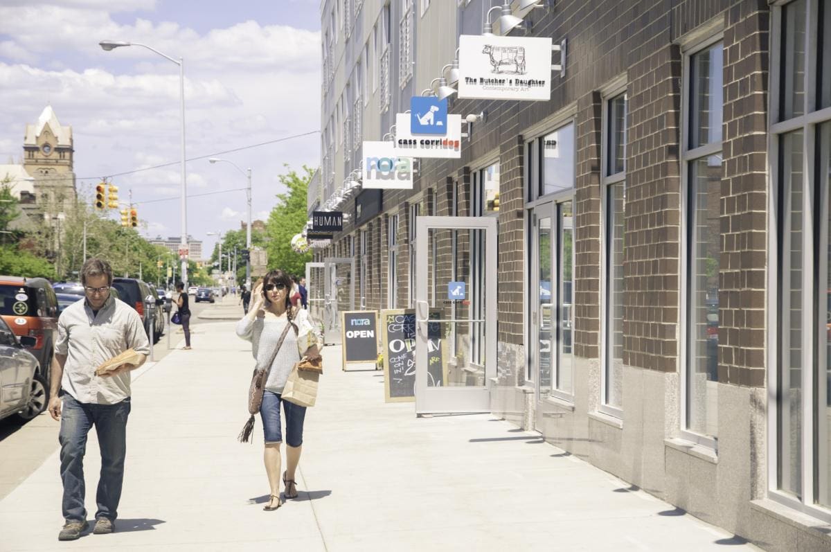 Photo of the crowd walking down a road lined with small stores and boutiques in Detroit on a sunny day.