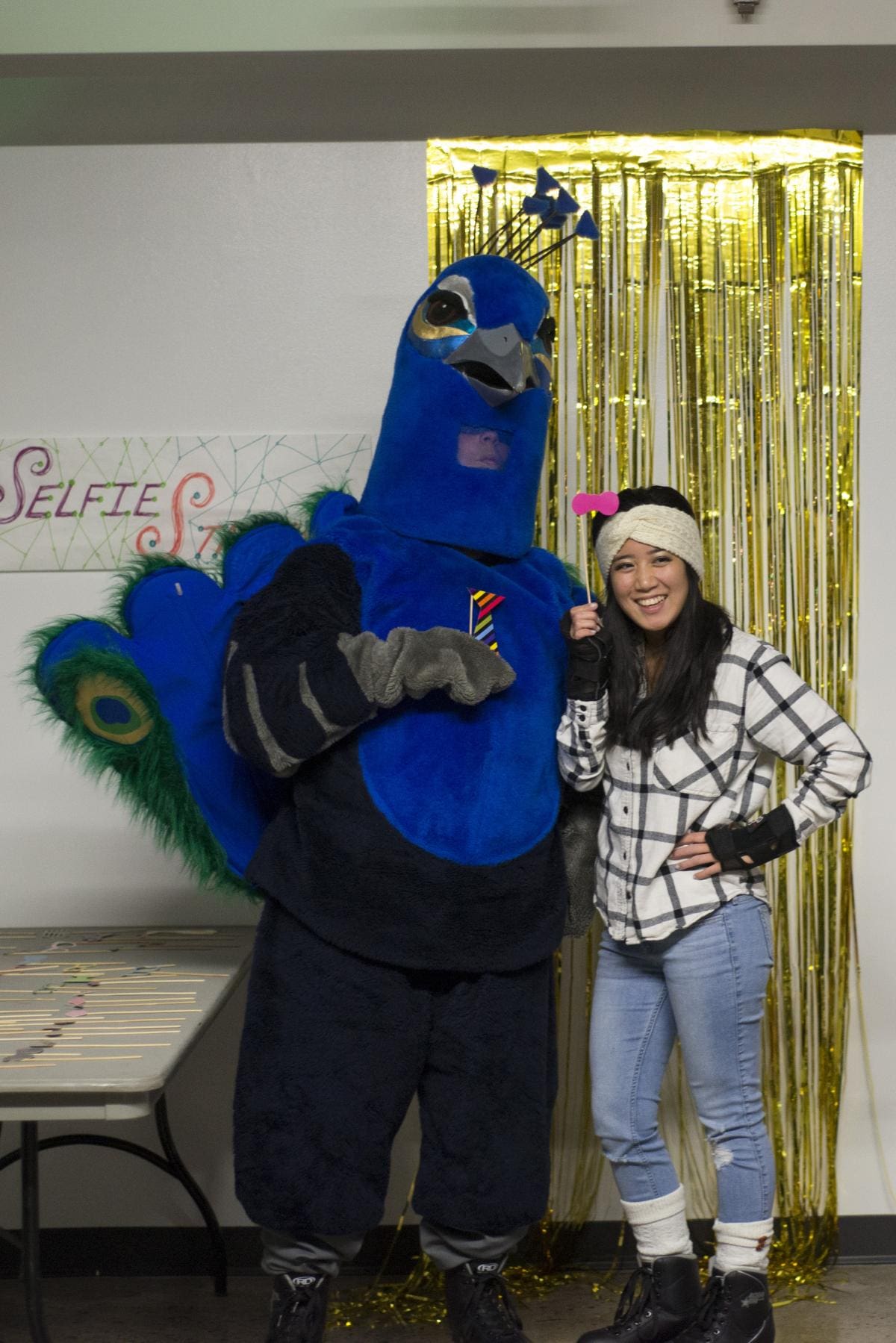 Photo of a lady dressed in autumn clothes smiling and posing for a photo with the CCS mascot, Watson the Peacock at a celebration.