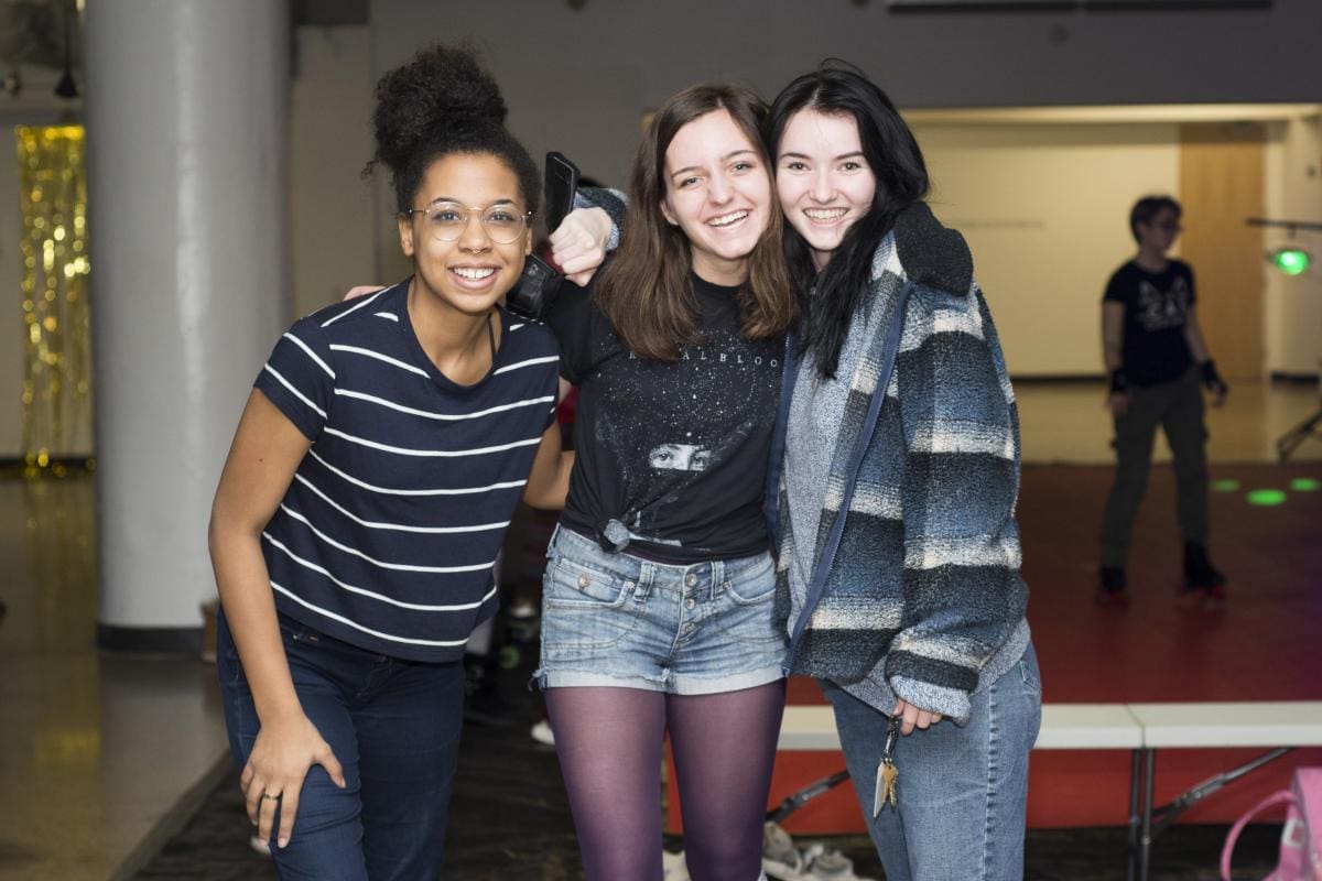 Photo of three CCS students smiling and embracing each other for a photo.