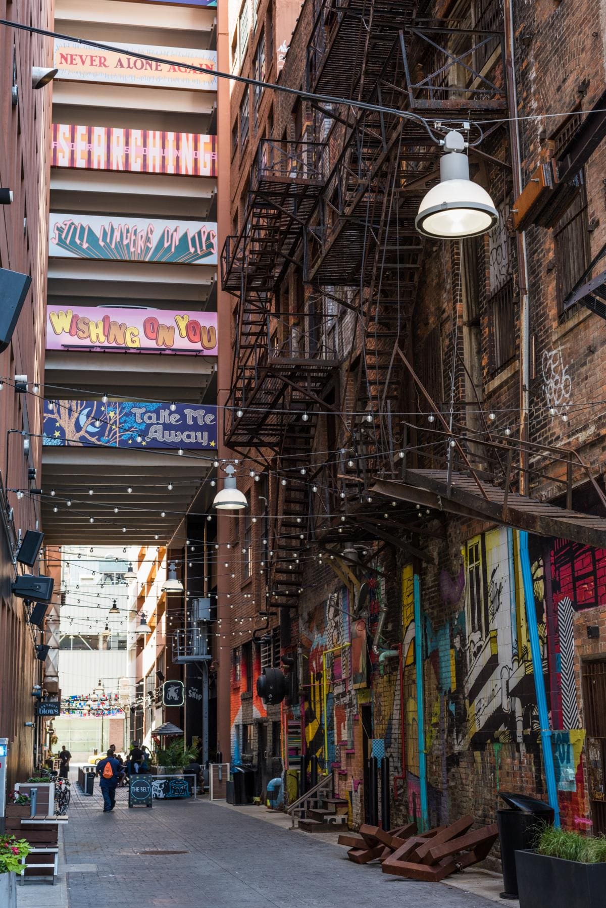 Photo of an alley in Detroit decorated with brightly colored murals and fairly lights.