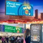 Three images showing different advertisements for Lays potato chips. The top shows a blue billboard above a busy street during night. Below is a huge green ceiling poster in a busy airport. There is also a grey poster on the side of a bus stop.