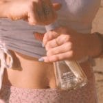 Close-up wide shot of someone in the desert, opening the cap of a clear plastic bottle with clear liquid soap inside.