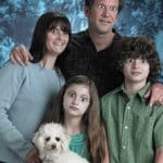 Photo of a family portrait posing in front of a blue background. The family includes a mom, dad, son, daughter, and white small dog. The family members' eyes have been replaced with white hearts with black circles in the center. White text at the bottom reads, "Your soup will satisfy the family."