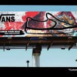 Photo of a billboard on a sunny day with a clear sky. The billboard shows a closeup photo of a lion graffiti mural. On top is a black outline of a shoe, and to the left is a black Vans logo and text that reads "Customize your Sole".