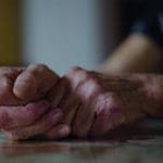 Closeup photo of an old woman's hands clasped together, resting on a table.