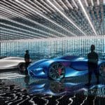 One blue and one white Maserati concept sports cars parked in a room lit up by multiple decorative lights.