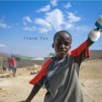 Picture of a smiling boy with a prosthetic arm in a third world country. Black text says "Thank you."