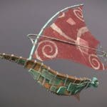 Digital rendering of a wooden windsurfer. The boat part is covered in green patches, and the sail is red with white swirls.