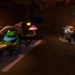 Digital rendering of a 3D animated scene. A frog character in a wide-brimmed hat and blue scarf sits at a table in a dimly lit underground cafe at night. The furniture is made of wood and stones, and there are low hanging ceiling lights providing a yellow glow to the scene.