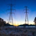 Photo of transmission towers in a field at dusk. The sky is deep blue with a faint yellow sunset.