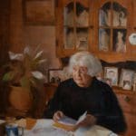 Portrait of an old woman sitting at her dining table, with a wooden cabinet of fine china behind her. She looks off into the distance with a book in her hands.