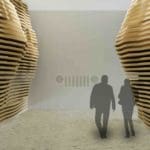 Photo of two people walking in an art exhibition surrounded by giant wavy wooden sculptures.