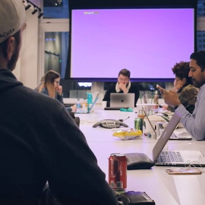 Five people sit around a table and work on their laptops in front of a large projector.