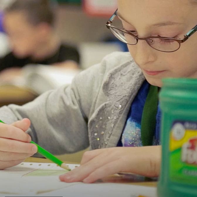 Close up photo of a child writing at their desk in school.