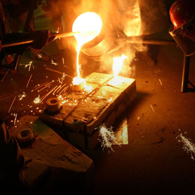 Close up photo of a metalsmithing student pouring molten metal into a mold.