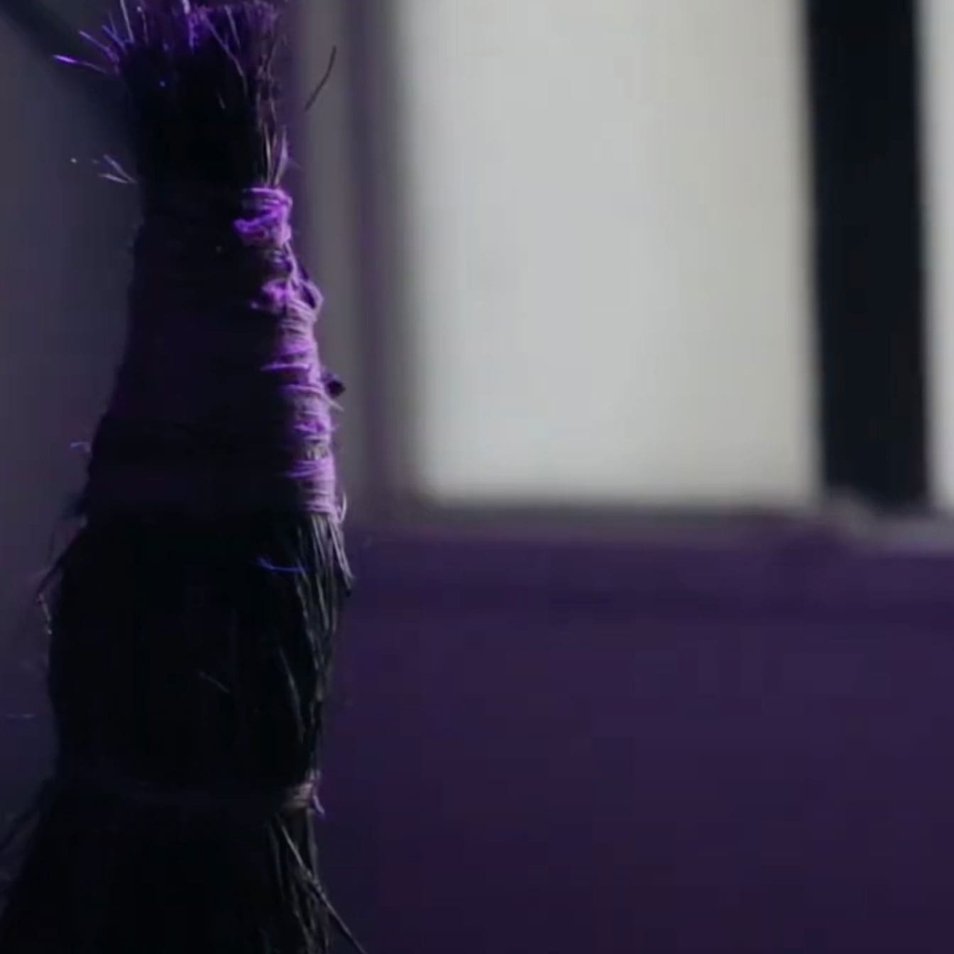 Close up photo of a long bundle of dried grass wrapped with purple yarn.