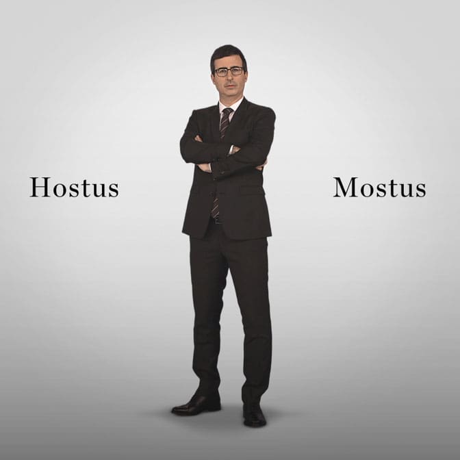 Photo of talk show host Jon Oliver wearing a black suit standing with his arms crossed against a white background. Black text says "Hostus Mostus".