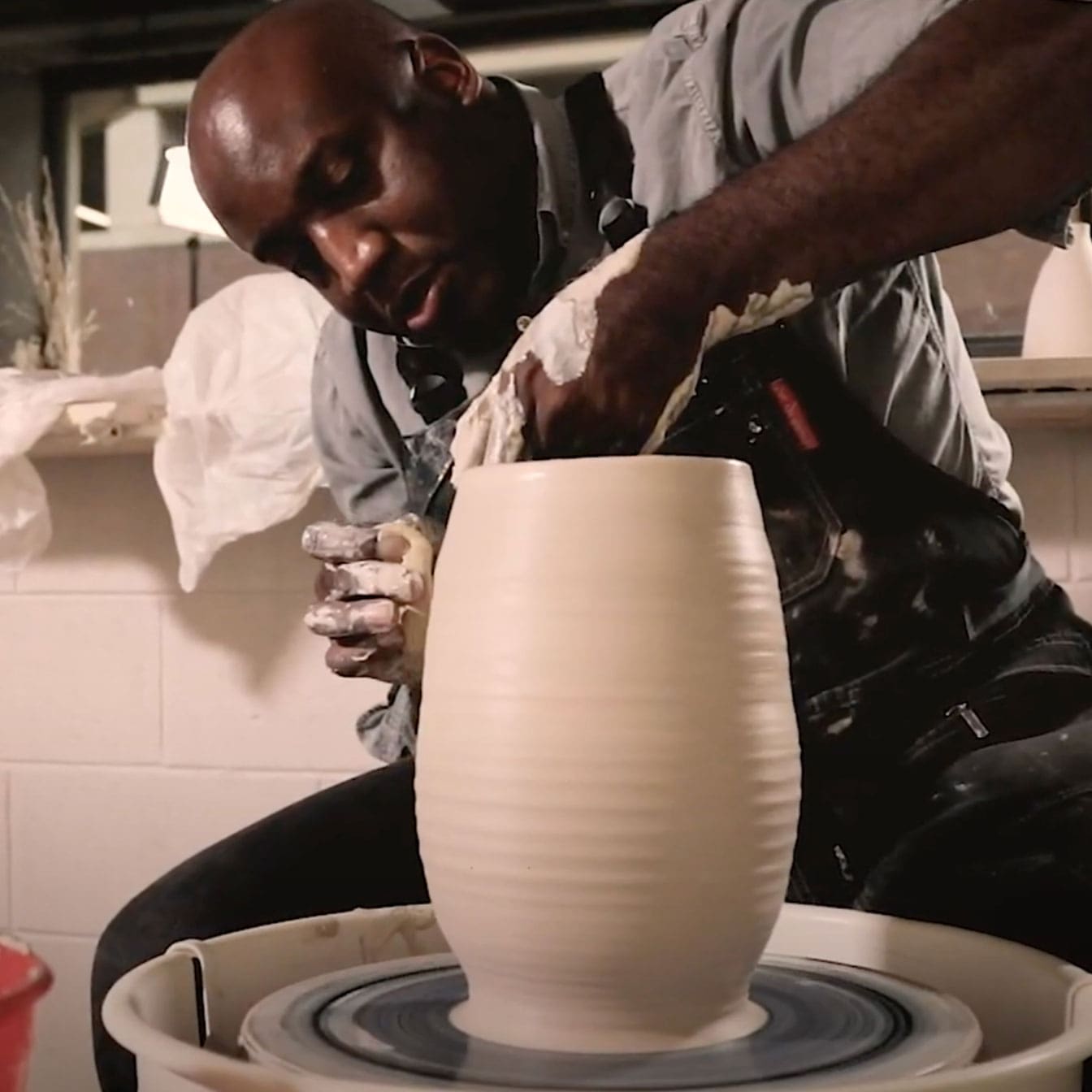 Photo of a man working on a clay vase on a pottery wheel