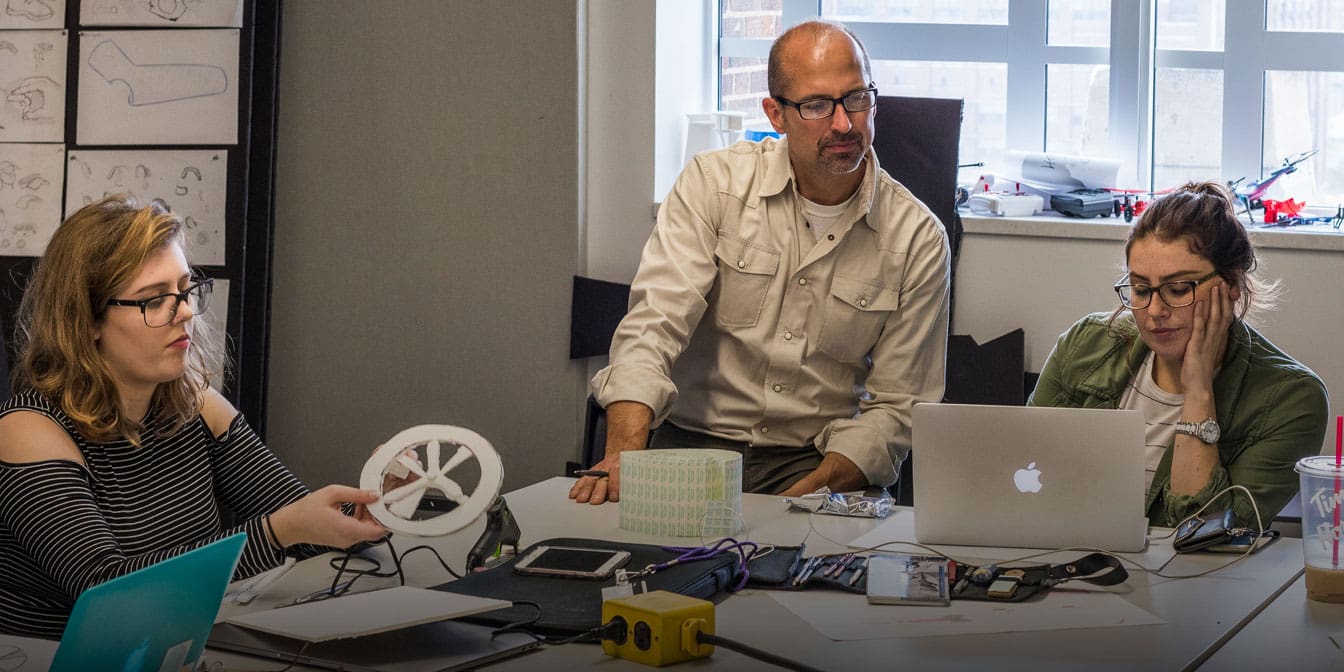 Photo of three people working with prototypes at a work table.