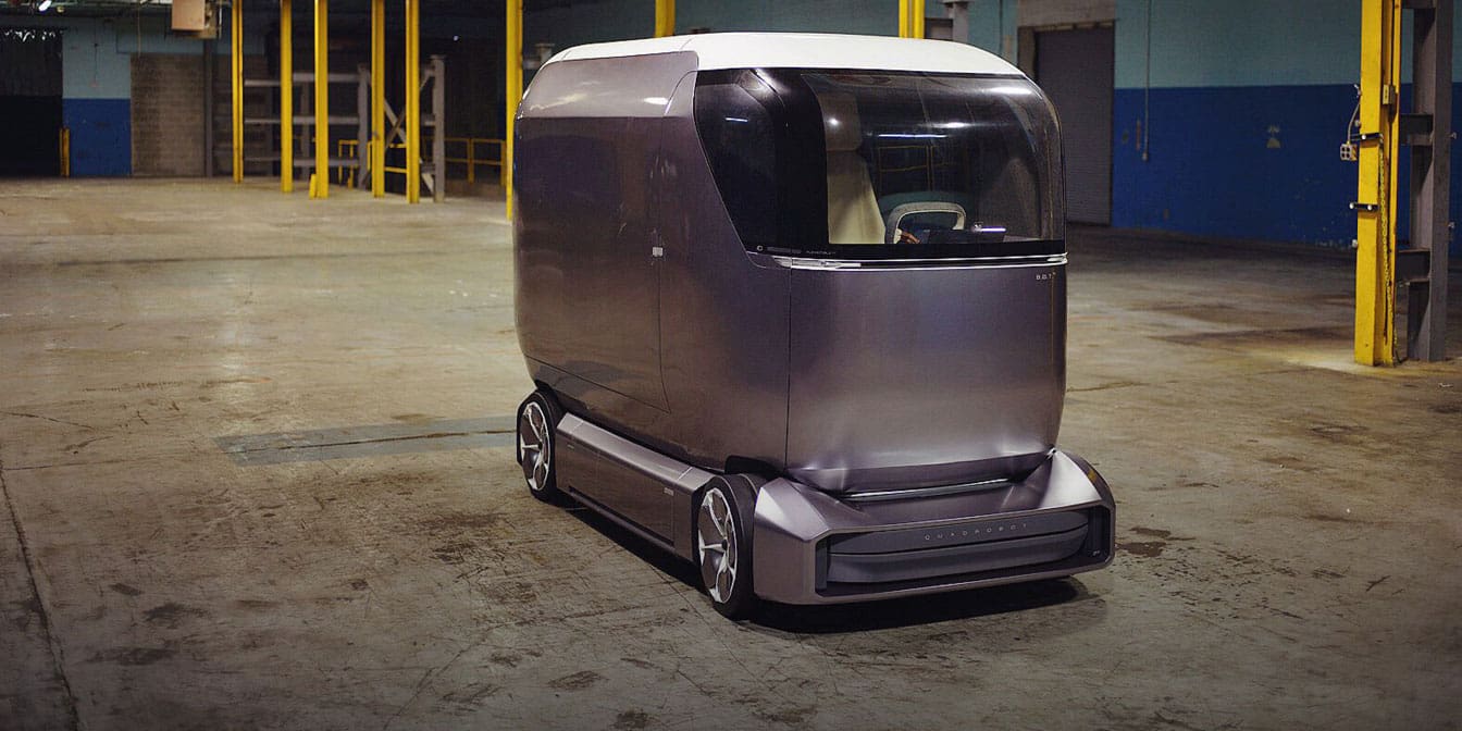 Photo of a silver, boxy futuristic vehicle in a mechanic's garage.