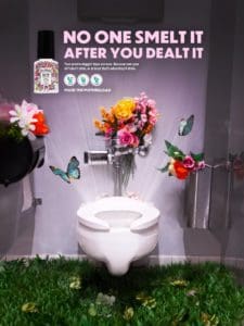 Print advertisement for poopourri depicting a toilet with flowers and butterflies bursting out of it. A pink tagline at the top reads "No one smelt it after you dealt it" 