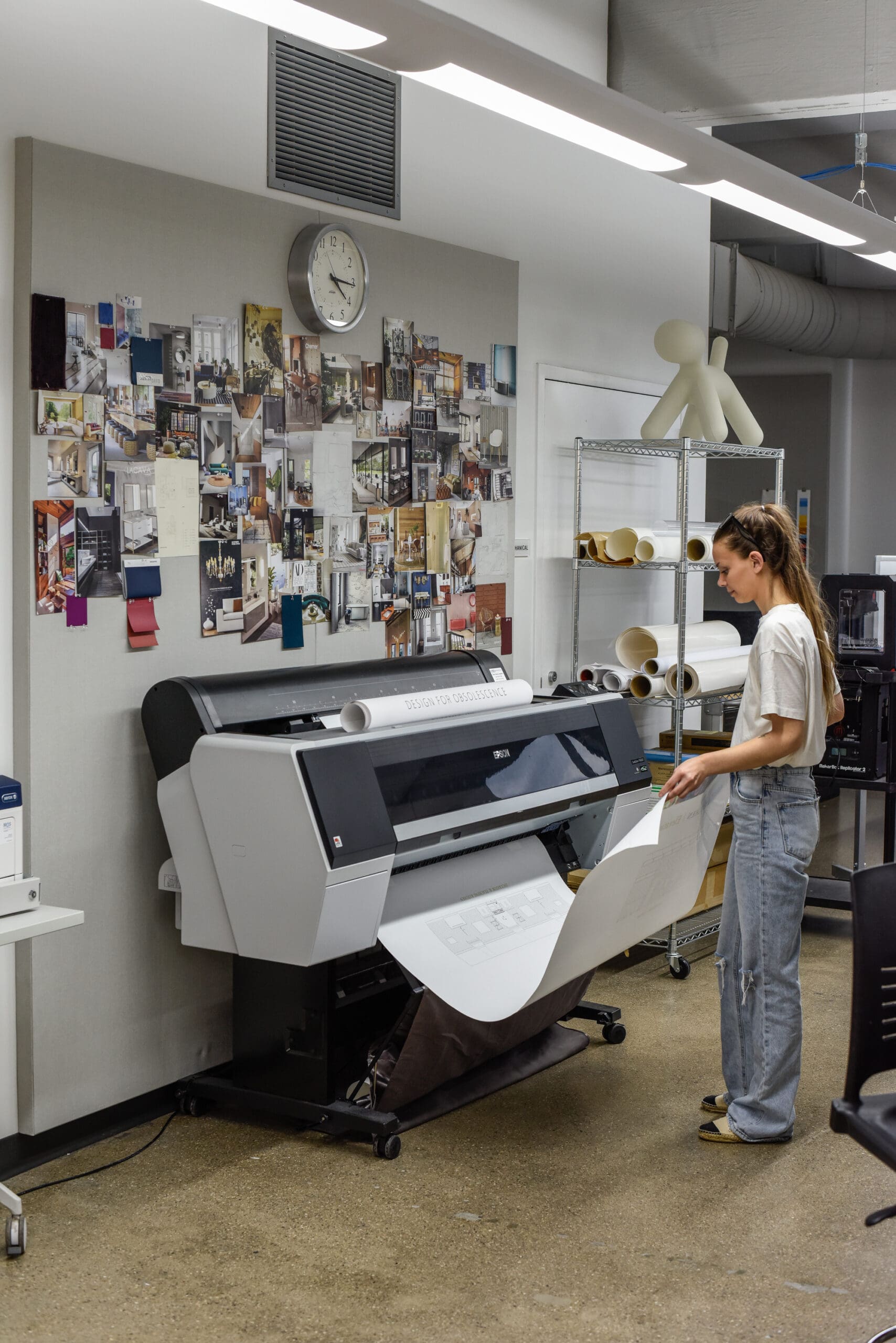 student in front of a large format plotter printer holding a large piece of paper