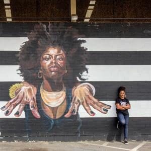 Photograph of artist Sydney James next to her mural outside