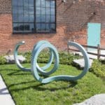 a teal colored sculpture made of metal placed outside of a building