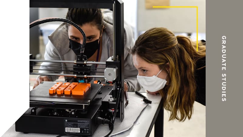 Two students looking very closely at a 3D printer at work.