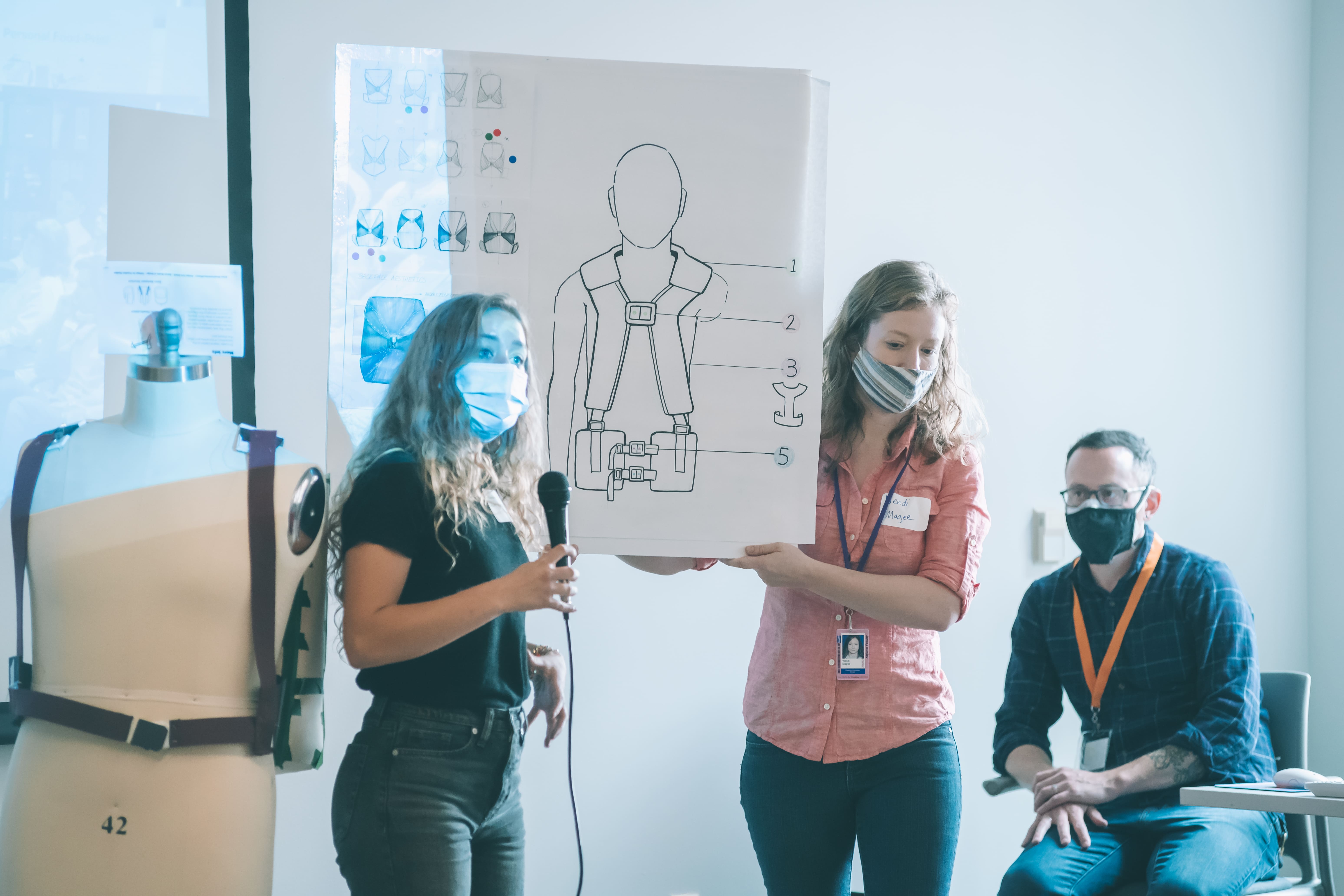 a photograph of two people presenting a poster of art and speaking on a microphone