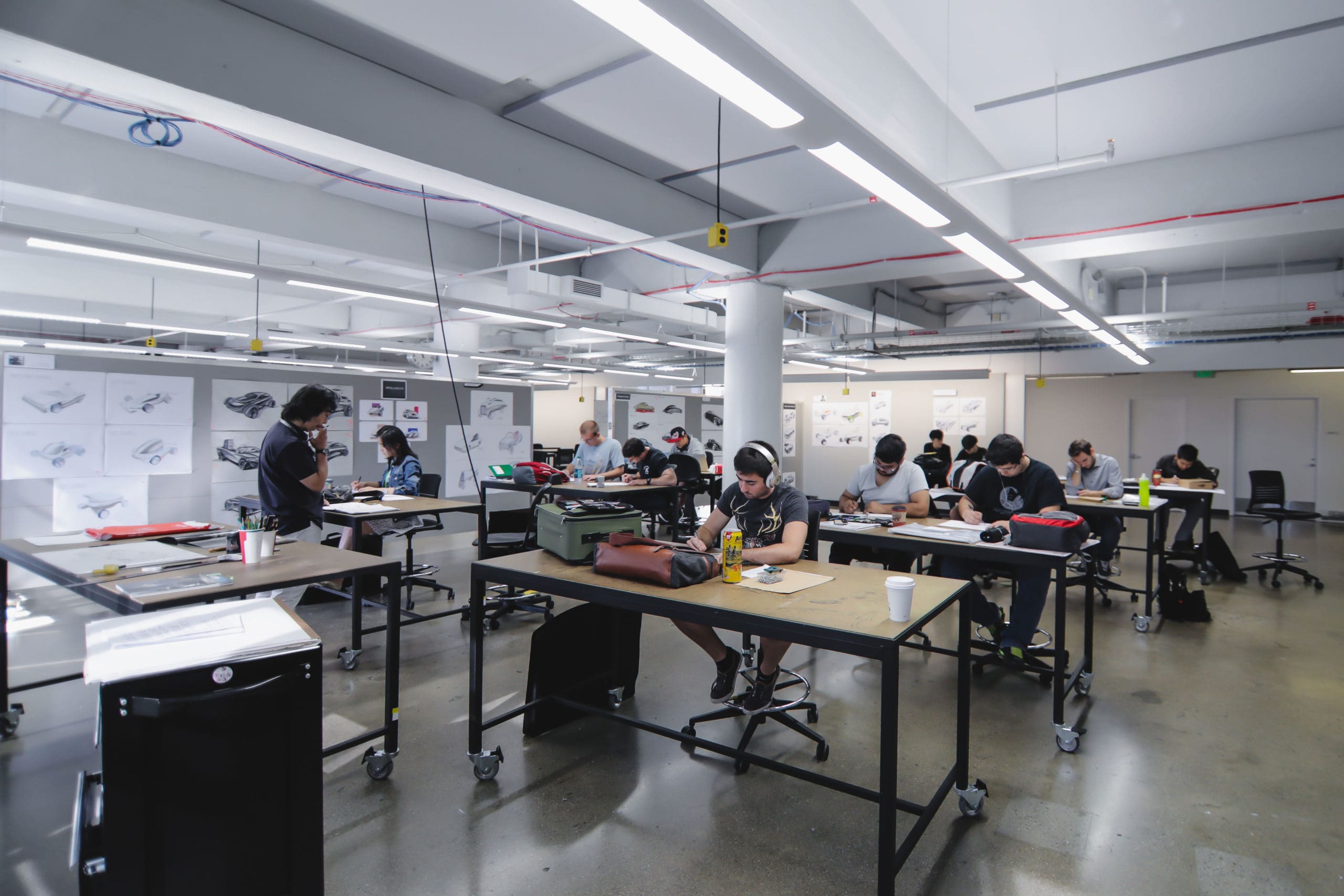 Students drawing in class at open worktables in the transportation Design studio