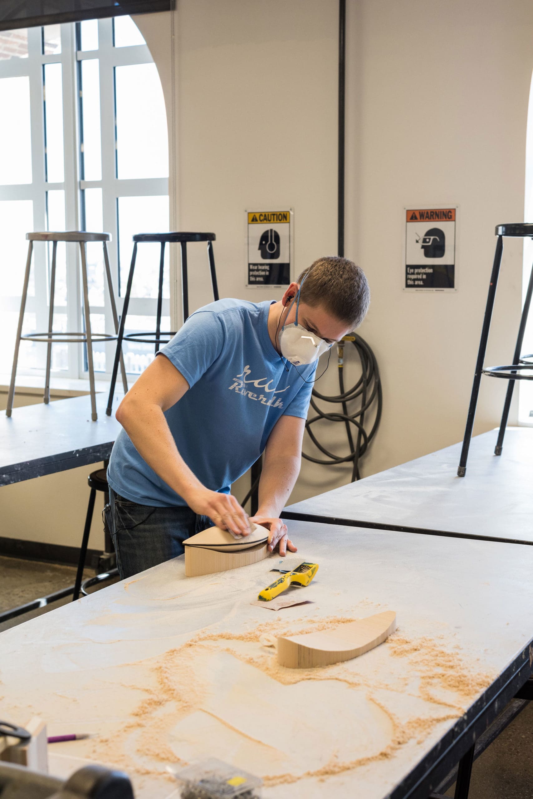 Image of a student sanding a piece of wood in a workshop for a transportation design class