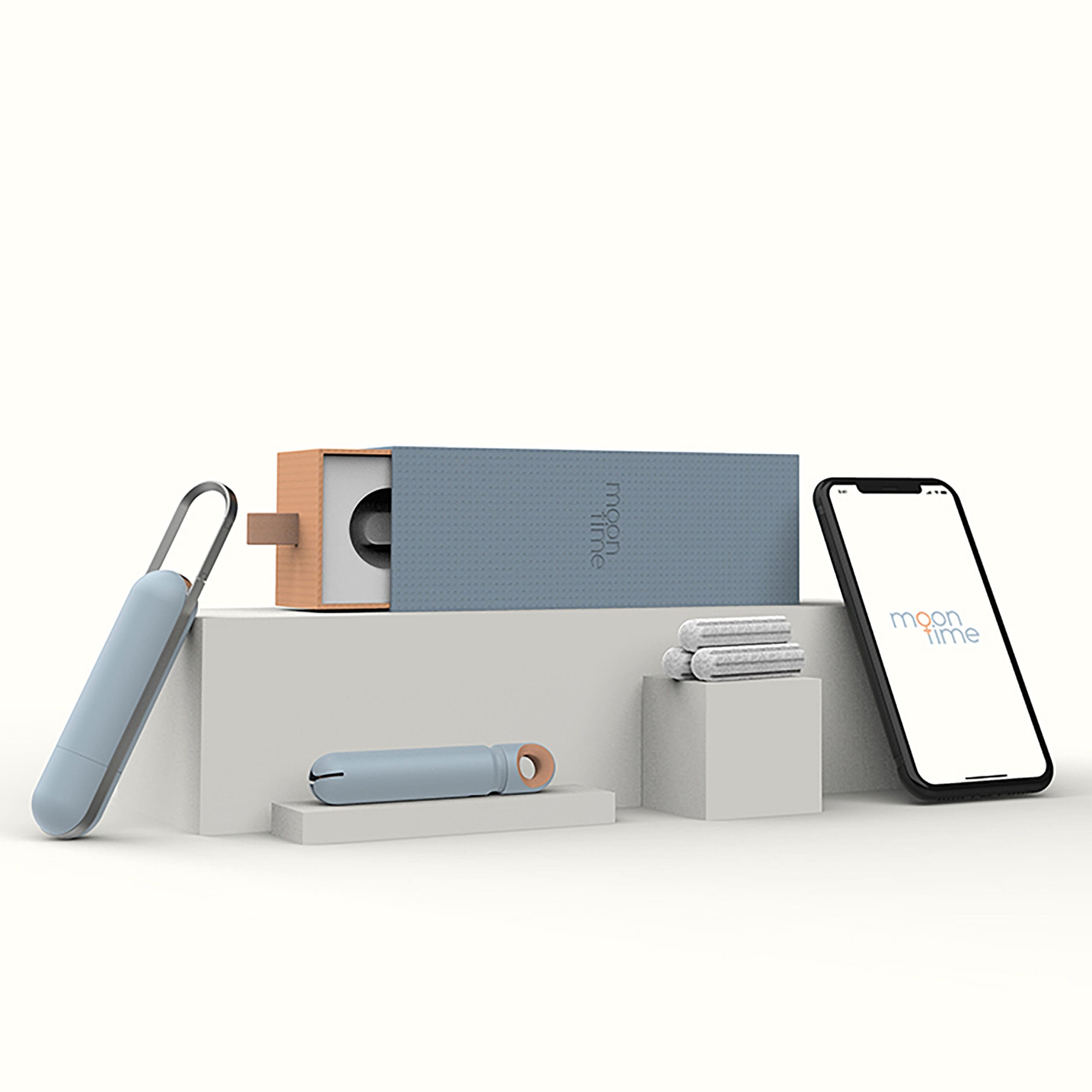 Photo of a smart phone, tampons in blue packaging, and other feminine hygiene products displayed on top of white blocks on a white backdrop. The phone and a long blue package says "Moon Time."