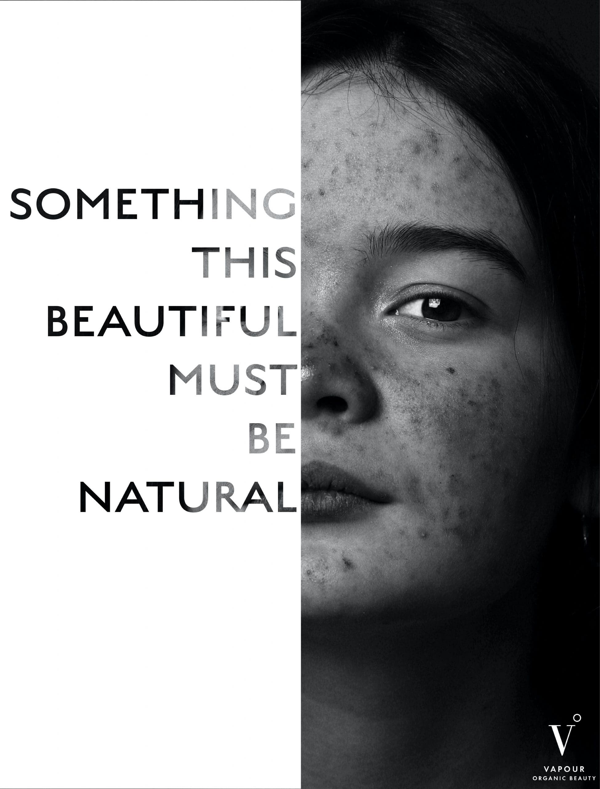 A black and white advertisement. The right side depicts half the face of a smiling women shown from the neck up, looking straight at the camera against a black background. The left side depicts a white screen with the phrase "Something This Beautiful Must be Natural".