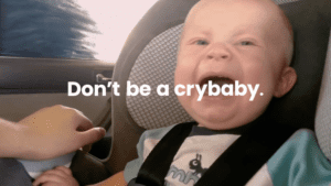 An advertisement that depicts a close up of a crying baby in a grey car seat. In the center is the phrase "Don't be a crybaby." in white text.
