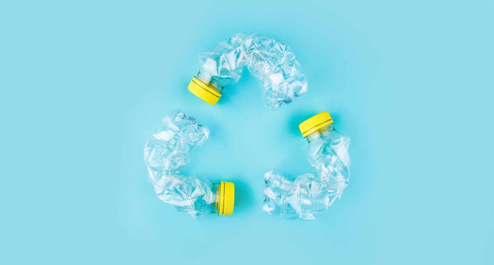 crushed plastic water bottles shaped in a recycling symbol with a light blue background