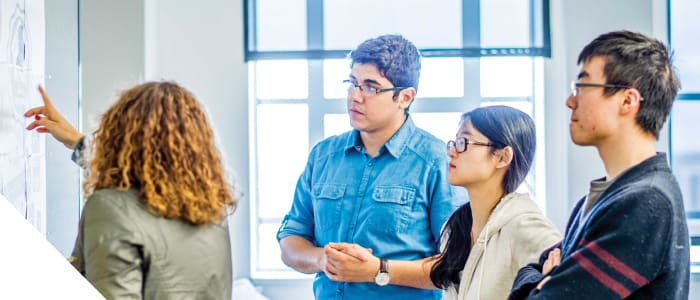 A CCS advisor pointing out things to a group of students on a whiteboard