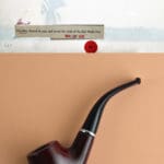 Art by Karen Larson titled Pipe. featured brown pipe on a bright orange background.