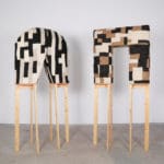 artwork of Ebitenyefa Baralaye.. Two arch-like sculptures made of black, tan and brown fabric squares balanced on top of wooden stilts.