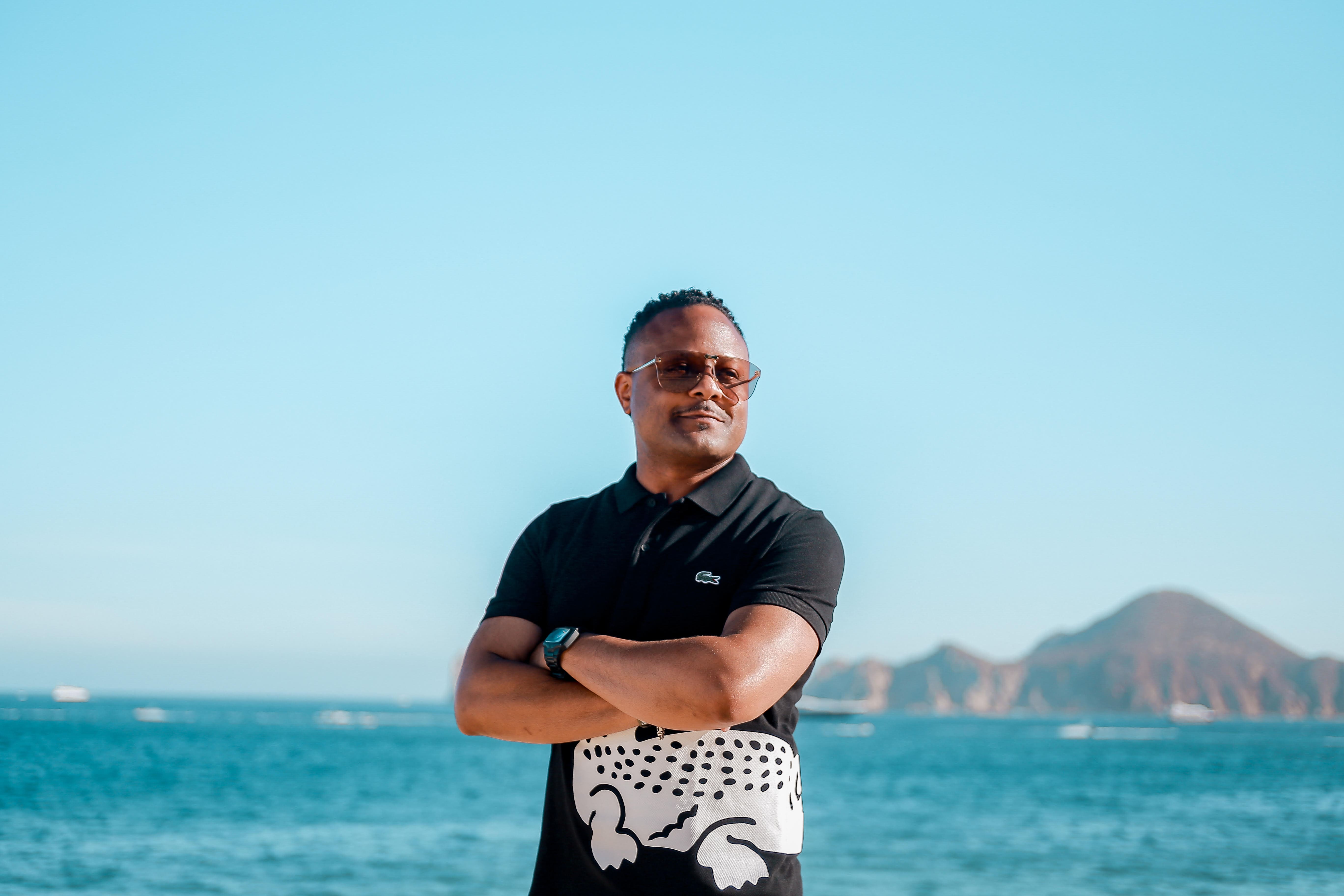 Antone Amye standing outdoors near a body of water and mountain in the distance