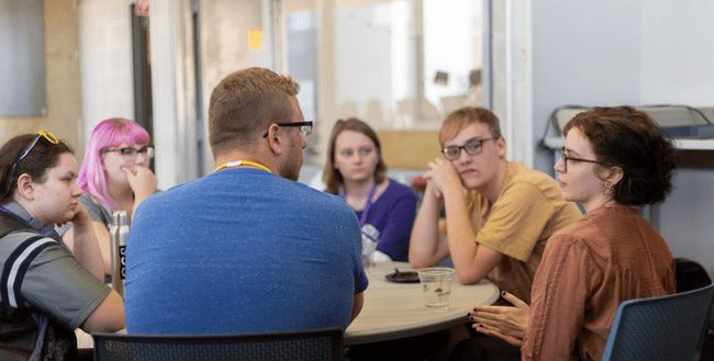 Untitled design (4) students gathered around a table speaking with a counselor