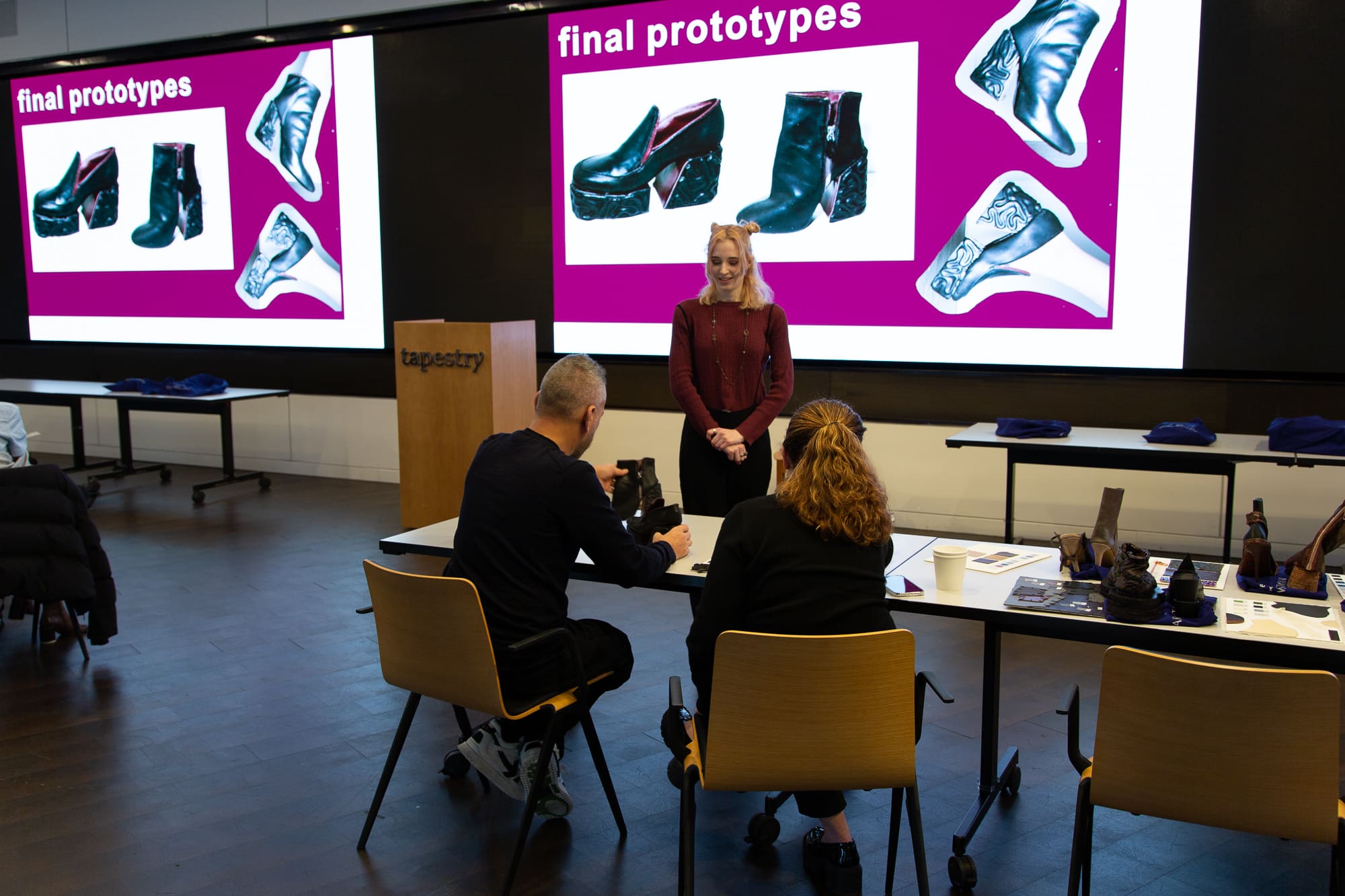 a student showing off shoe prototypes to a group of industry professionals