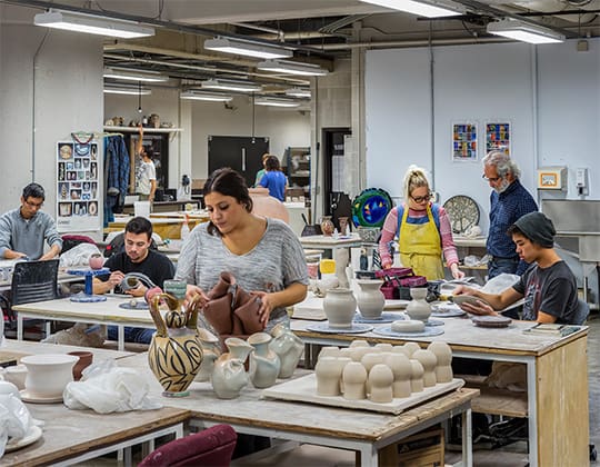 a ceramics class - students making pieces and speaking to faculty with finished pieces of ceramics sitting on tables
