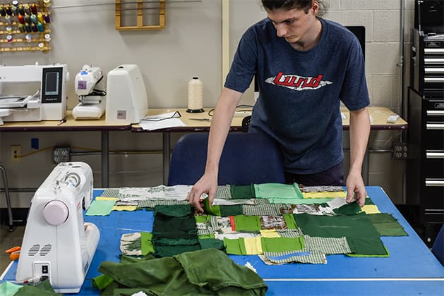 Student laying out pieces of green fabric in a quilt formation near a sewing machine