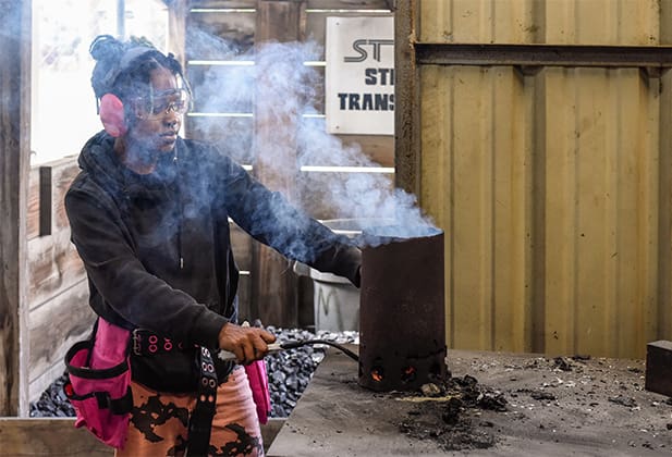 A student lighting a cylinder container with smoke coming from the top in the foundry