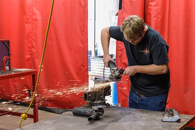 sparks fly as a student uses a saw on metal in the metalsmithing studio